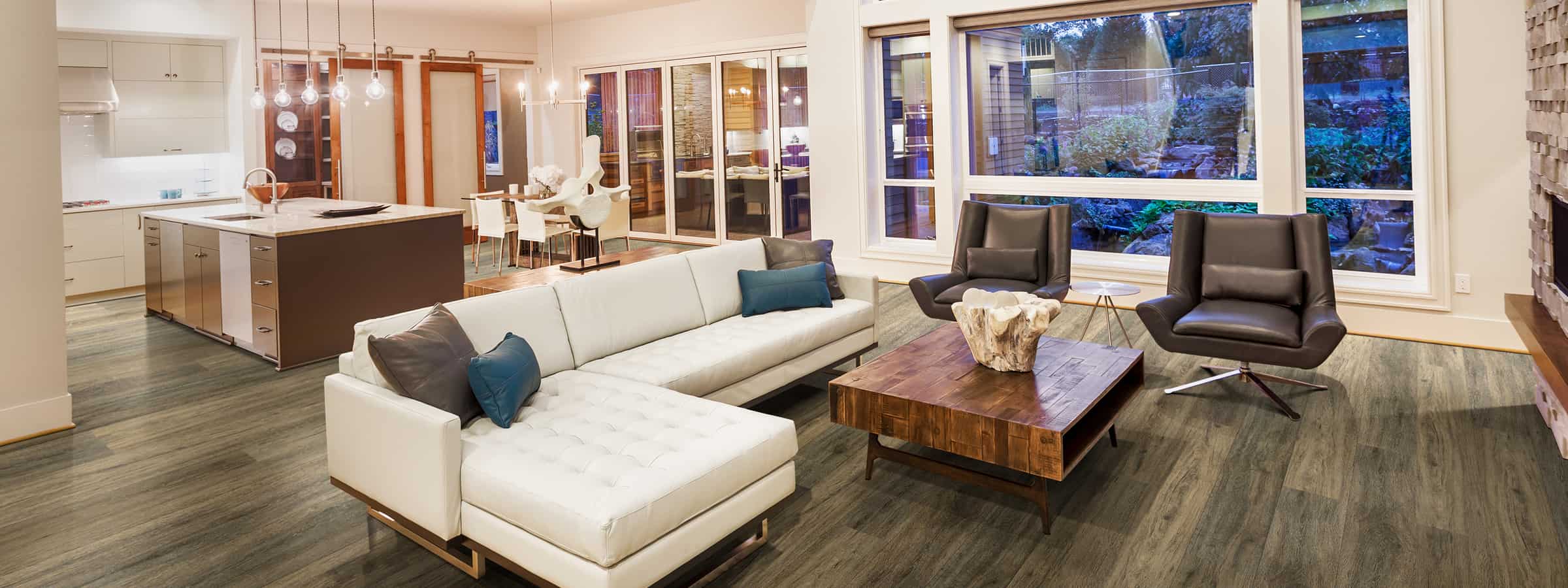 Soft modern living room with wood flooring, sleek furniture, and large windows showcasing a garden outdoor view.