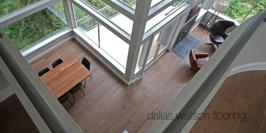 Shaded view of a modern living space with hardwood flooring and large windows, showcasing Dallas Watson Flooring craftsmanship.