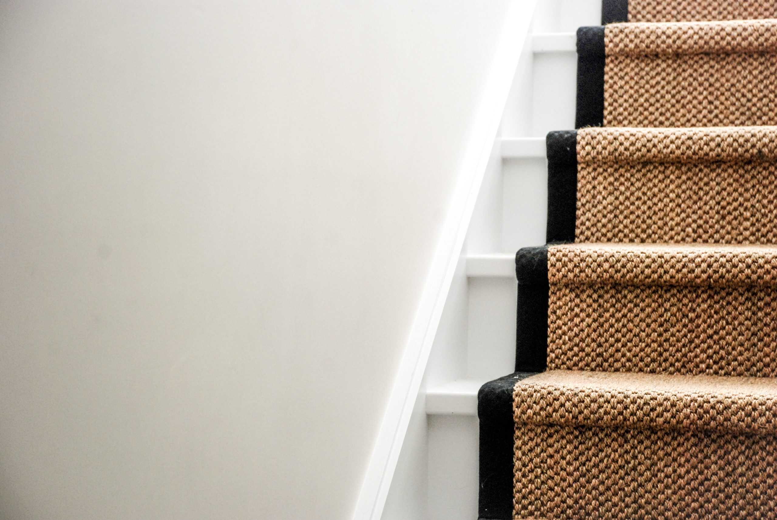 Brightly lit staircase with beige carpet runners and black trim, showcasing professional flooring installation.